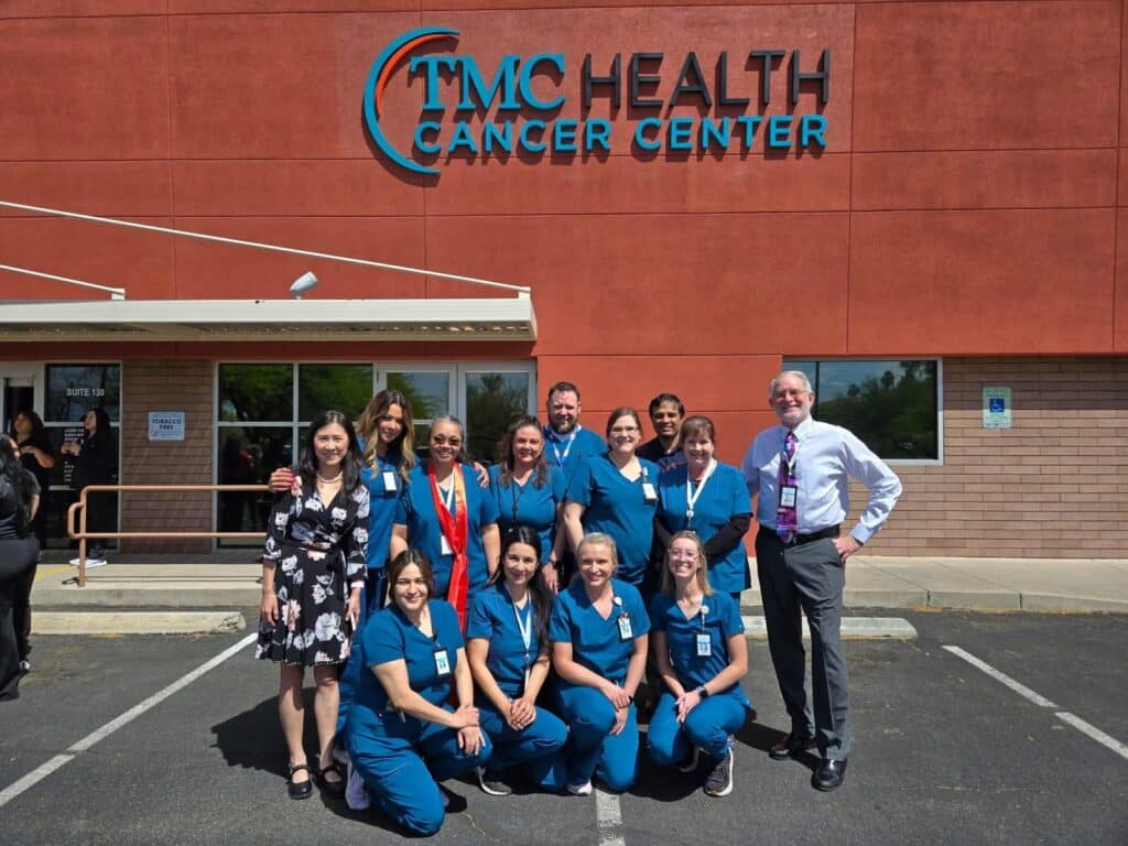 Two women smiling while holding a newborn baby, with one woman wearing medical scrubs in a hospital setting.