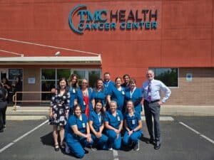 Two women smiling while holding a newborn baby, with one woman wearing medical scrubs in a hospital setting.